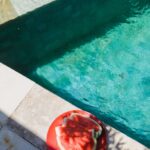 From above of small red slices of watermelon on round plate next to turquoise swimming pool in sunlight