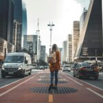photography of woman walking in between road with vehicles