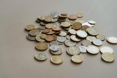 A variety of coins scattered on a neutral surface in soft lighting.
