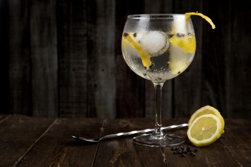 A close-up of a refreshing gin cocktail with lemon slices on a rustic wooden table, perfect for summer.