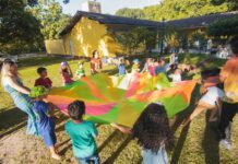 Campobello di Licata, “La Festa dell’Estate, la piu’ colorata” A lively group of children joyfully playing with a colorful parachute at an outdoor summer gathering.