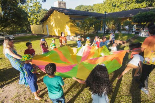 A lively group of children joyfully playing with a colorful parachute at an outdoor summer gathering.