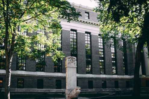 Exterior view of a university building with a stone statue and surrounding trees.