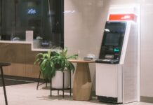 Burnout, allarme in Sicilia: nelle banche cresce il disagio psicologico An ATM machine stands in a modern bank lobby, next to a plant and table.