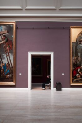 Art gallery in Rouen, France featuring large paintings and a curator seated in doorway.