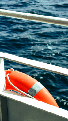 Orange lifebuoy hanging on a boat railing with the ocean in the background.